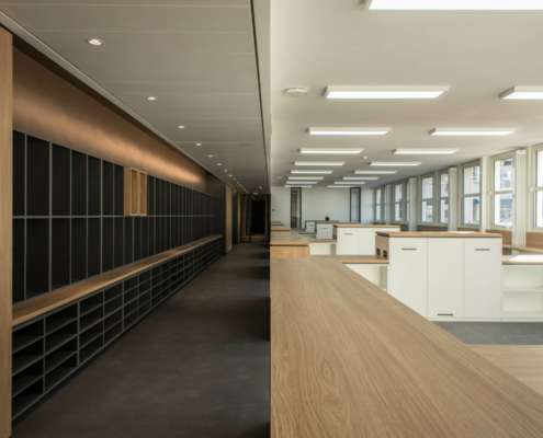 Vue en enfilade entre mur de casiers et plateau de bureaux éclairé, SAV Horlogerie Chanel ; conception lumière Ponctuelle