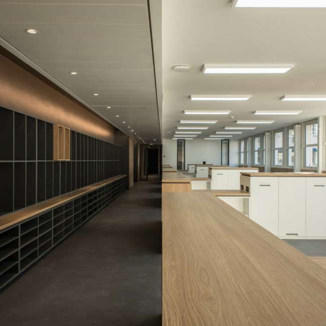 Vue en enfilade entre mur de casiers et plateau de bureaux éclairé, SAV Horlogerie Chanel ; conception lumière Ponctuelle