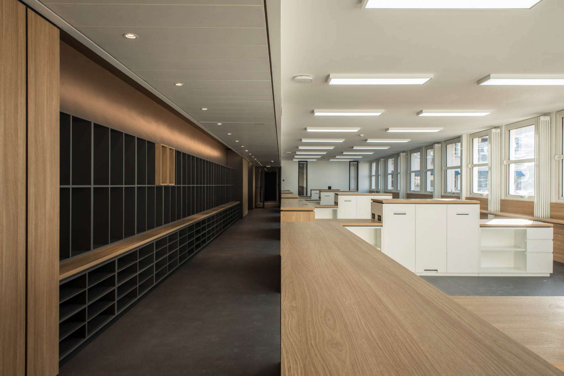 Vue en enfilade entre mur de casiers et plateau de bureaux éclairé, SAV Horlogerie Chanel ; conception lumière Ponctuelle