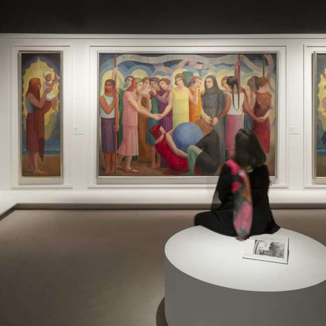 Salle d'exposition Art Déco France avec toiles figuratives éclairées et visiteuse assise, conception lumière Ponctuelle