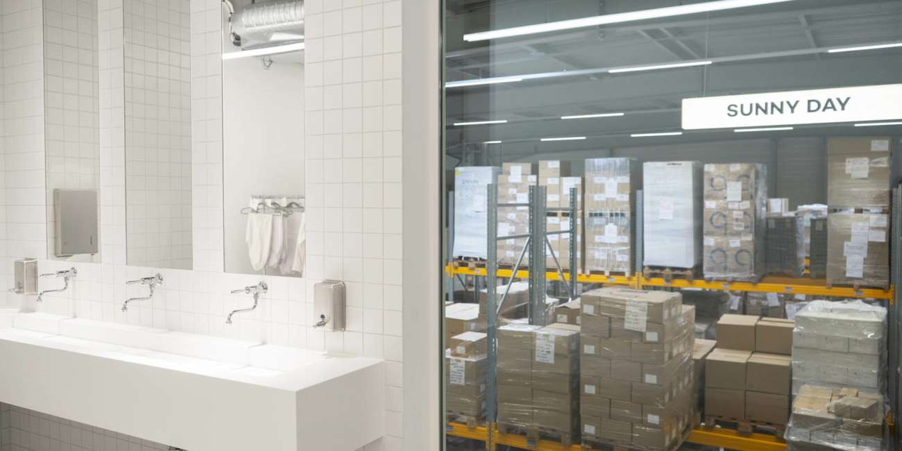 Vestiaire carrelé avec vasque en résine face à une zone de stockage logistique, D-LAB Industry conception lumière Ponctuelle