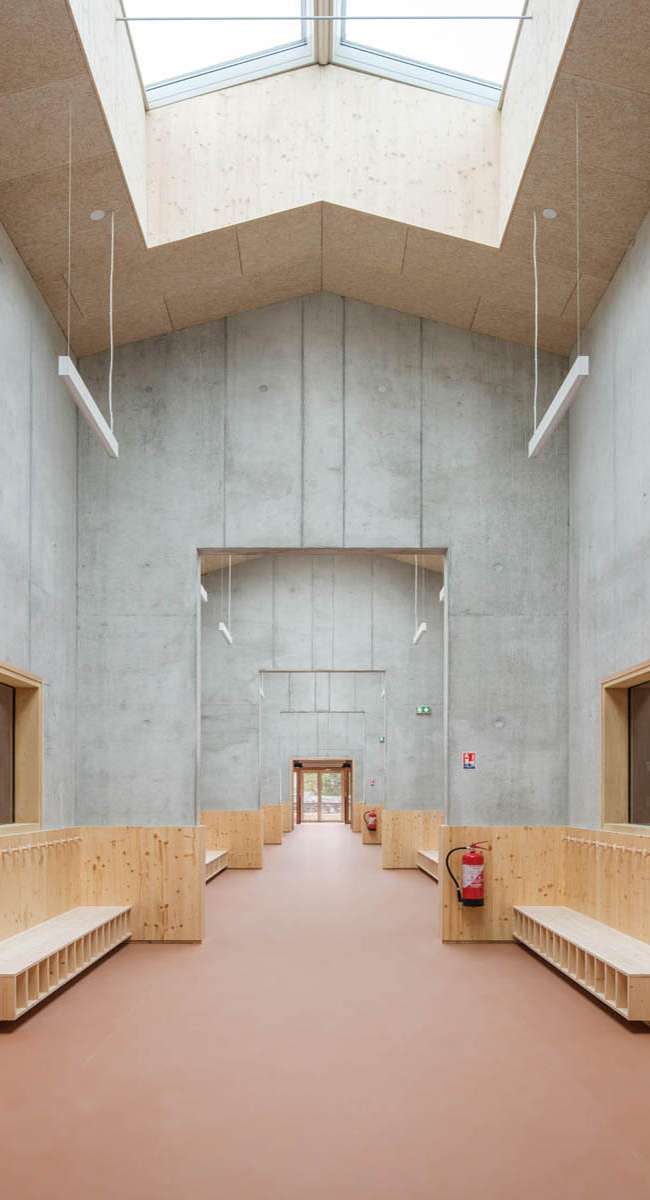Vestiaire d'école sous verrière zénithale, suspensions lumineuses et bancs en bois, conception lumière Ponctuelle
