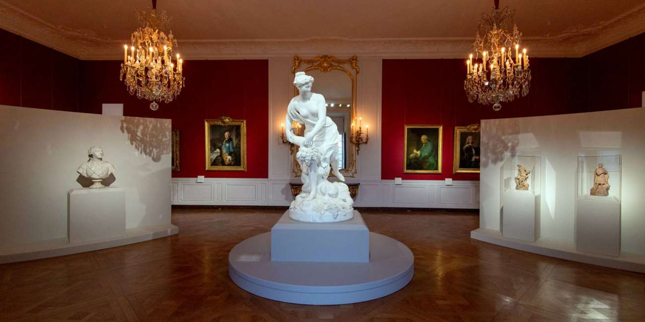 Salon rouge avec lustres à bougies et sculpture en marbre, exposition Trésors retrouvés au Château de Versailles, conception lumière Ponctuelle