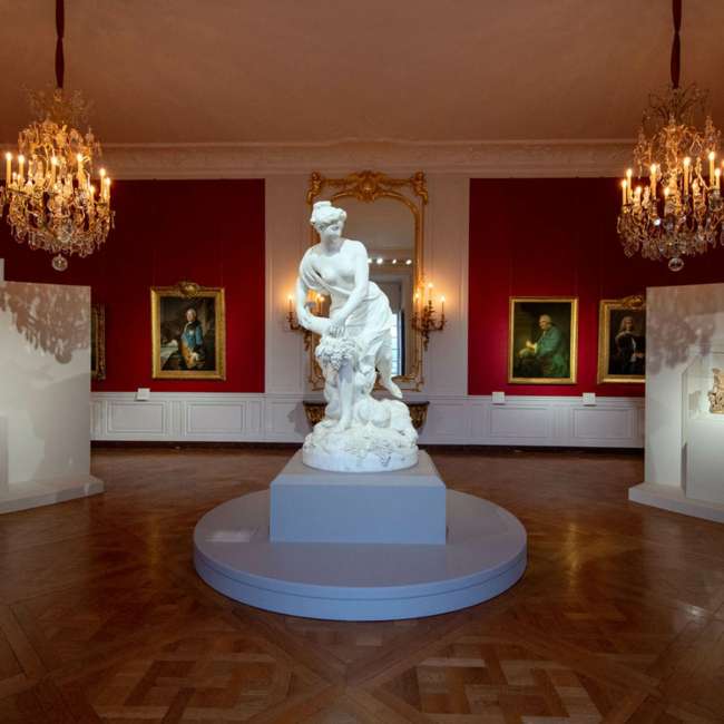 Salon rouge avec lustres à bougies et sculpture en marbre, exposition Trésors retrouvés au Château de Versailles, conception lumière Ponctuelle