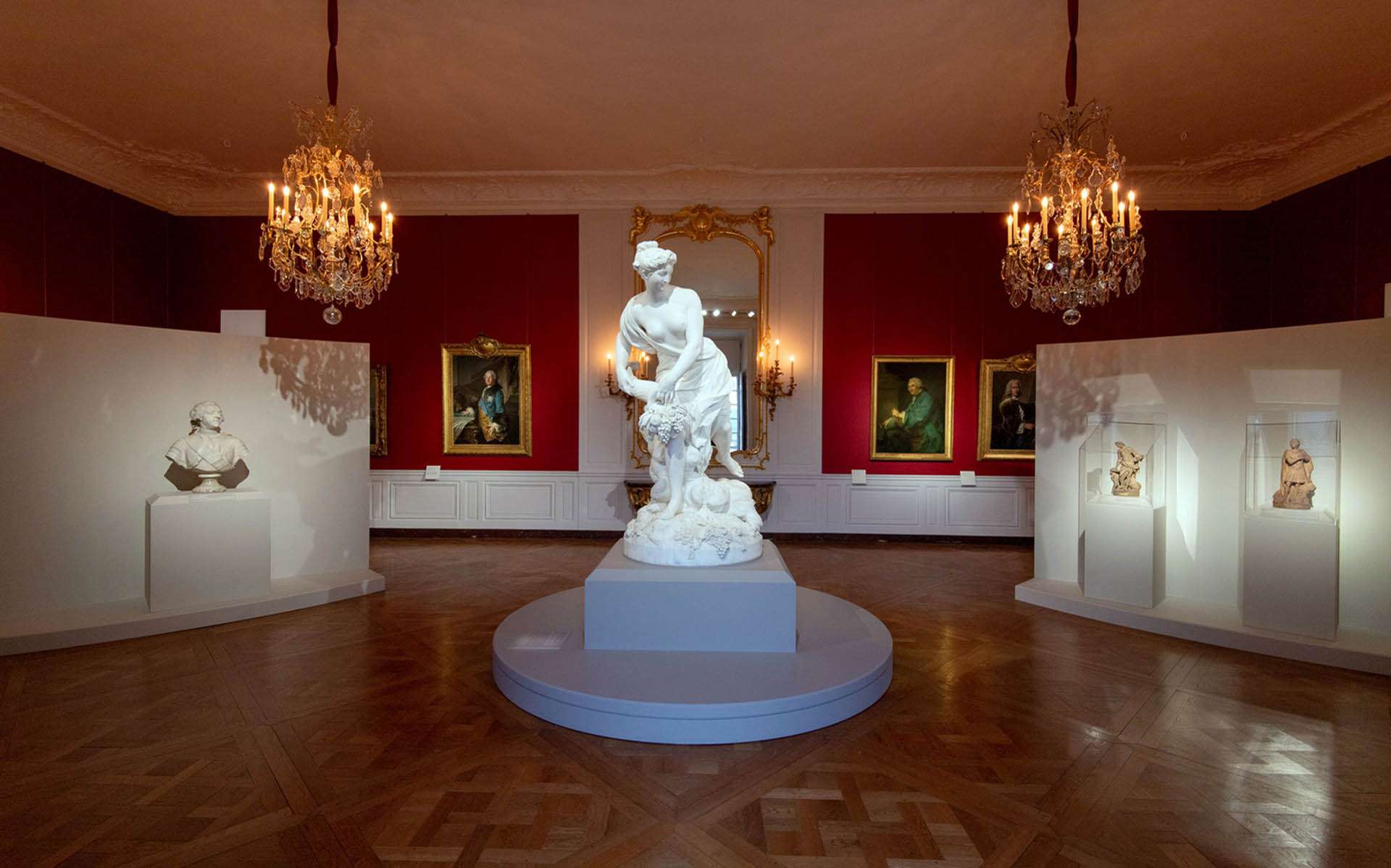 Salon rouge avec lustres à bougies et sculpture en marbre, exposition Trésors retrouvés au Château de Versailles, conception lumière Ponctuelle