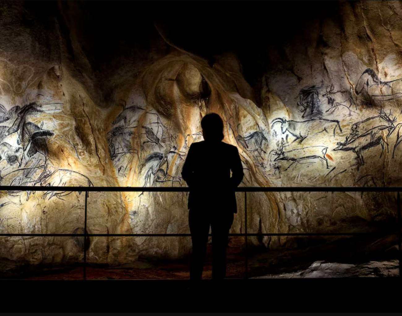 Visiteur en silhouette face aux fresques rupestres éclairées de la reconstitution de la grotte Chauvet, conception lumière Ponctuelle