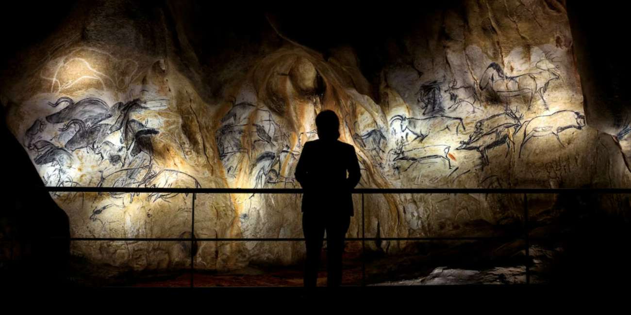 Silhouetted visitor facing the illuminated cave paintings in the replica of the Chauvet Cave, lighting design by Ponctuelle