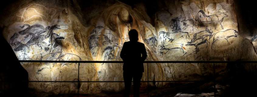 Visiteur en silhouette face aux fresques rupestres éclairées de la reconstitution de la grotte Chauvet, conception lumière Ponctuelle