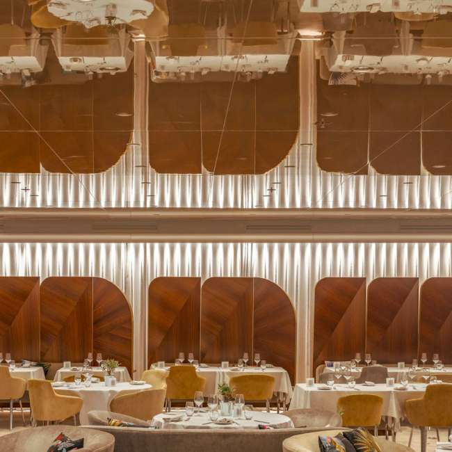 Restaurant du JW Marriott Cannes avec panneaux en bois cintrés et éclairage indirect entre les niveaux, conception lumière Ponctuelle
