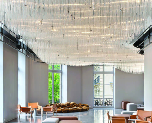 Hall d'accueil sous un lustre monumental en tubes de verre suspendus, mise en lumière L'Oréal Le Visionnaire