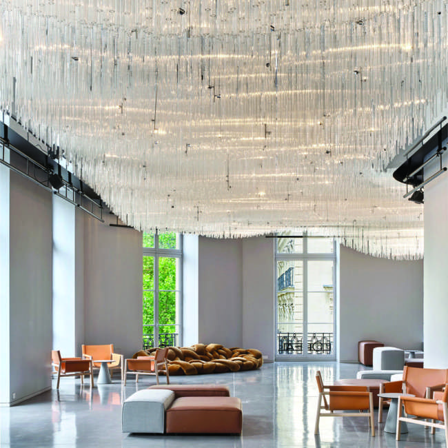 Hall d'accueil sous un lustre monumental en tubes de verre suspendus, mise en lumière L'Oréal Le Visionnaire