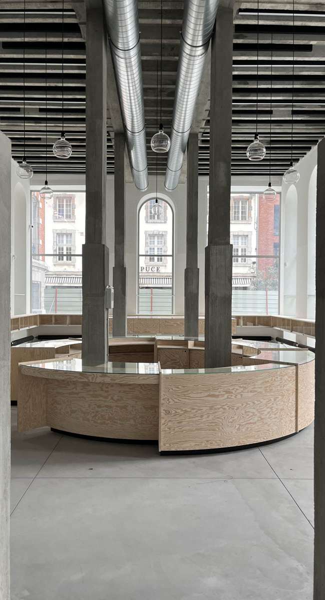 Hall du Smart Center de Tournai avec comptoir circulaire en bois et suspensions en verre, conception lumière Ponctuelle