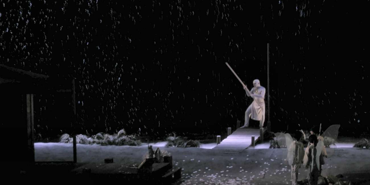 Personnage bâton levé sur le ponton sous une pluie nocturne éclairée en contre-jour, Madame Butterfly, Opéra de Marseille, conception lumière Ponctuelle