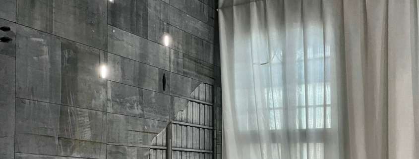 Lighting design for the Smart Center in Tournai: raw concrete wall punctuated with recessed lights and a white voile curtain in natural light