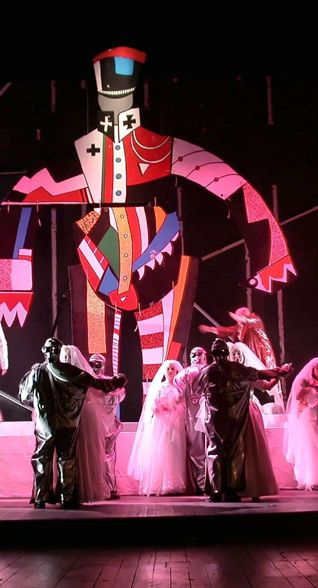 Marionnette géante colorée dominant un chœur en voiles blancs et costumes sombres sous lumière rose, Wozzeck, Opéra de Nantes, conception lumière Ponctuelle